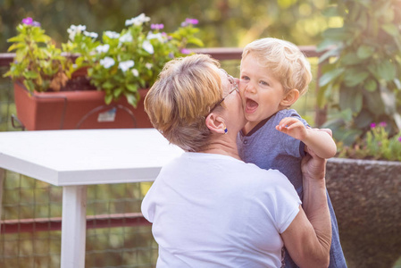 祖母拥抱和温柔地亲吻她的孙子在庭院, 自然光