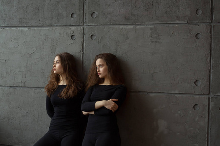 两个美丽的双胞胎姐妹的肖像与流动的头发对灰色的墙壁在内部