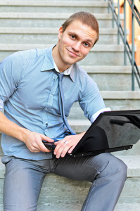 年轻的小伙子坐在楼梯上的一台笔记本电脑