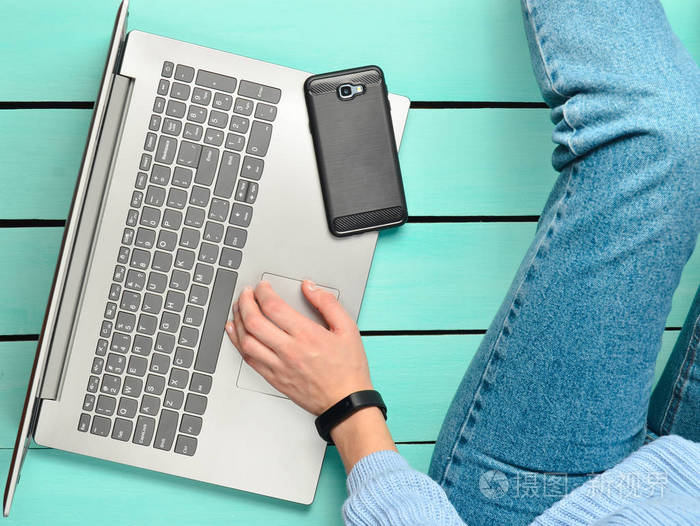 一个现代的女孩坐在蓝色的木地板上, 并使用笔记本电脑。世代 z。自由职业者的概念。工作空间。顶部视图