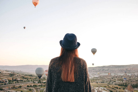 一个戴着帽子的旅游女孩羡慕在土耳其上空飘扬的热气球。令人印象深刻的景象