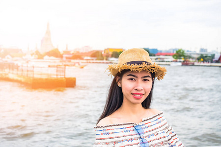 亚洲女子旅游戴着帽子站在微笑的背景是朝阳河和宝塔阿伦寺的地标和景点泰国曼谷