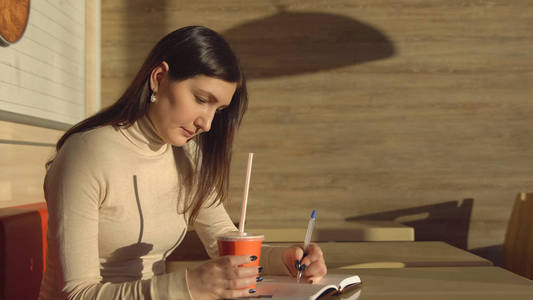 咖啡馆里的年轻女人在笔记本上做笔记, 喝果汁。