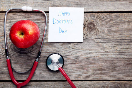 用听诊器和红苹果在木桌上题词快乐医生日
