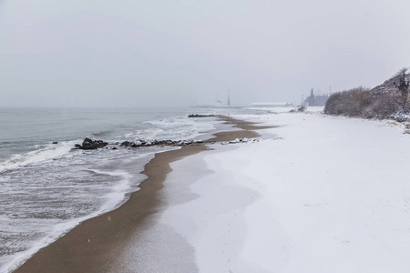 海滩的风景在冬天时间。白色蓬松的雪而不是黄色的细沙。海港背景下的雪景