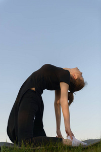 穿黑色衣服的女孩在蓝天上练习瑜伽