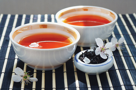 两杯茶,罐茶叶和樱花竹表布上照片