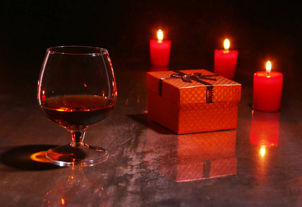 圣诞节装饰。木制背景下的白兰地或威士忌, 红色蜡烛和礼品盒玻璃