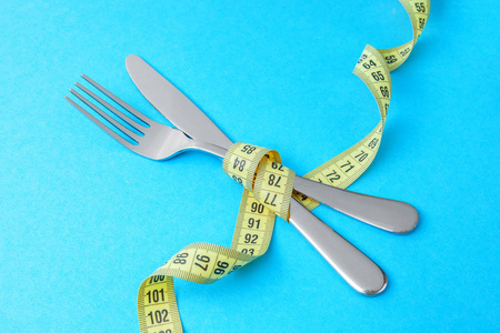 低卡路里饮食减肥。在蓝色背景下用黄色卷尺包裹刀叉