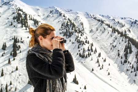 美丽的女孩看通过望远镜在雪山背景下