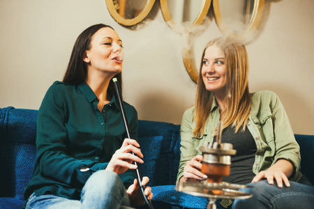 两个快乐的女人坐在水烟酒吧和吸烟 nargile