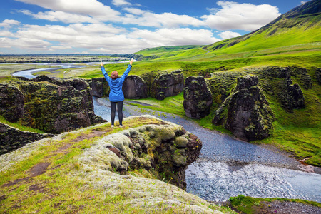 老妇人游客穿着蓝色夹克, 欣赏壮丽的景色。绿色的苔原在夏天。北方旅游活动的概念。冰岛惊人的峡谷