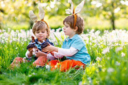 两个小男孩的朋友在复活节兔耳朵吃巧克力蛋糕和松饼