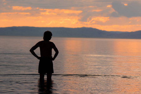 一个穿短裤的男人的剪影, 它站在大海的水中, 看着日落。
