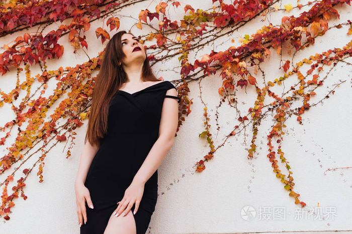 一个奢华的富有的女人穿着时髦的黑色礼服, 在花园里摆着墙, 休息和放松