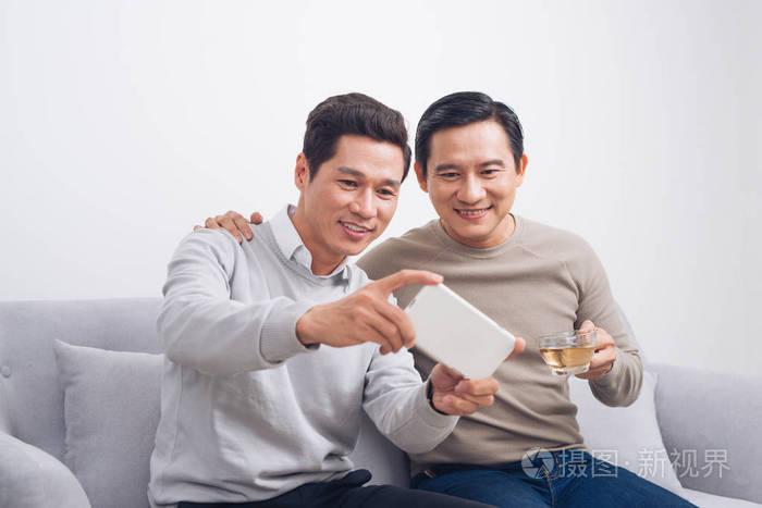 两个男性朋友玩游戏的智能手机坐在沙发上在家