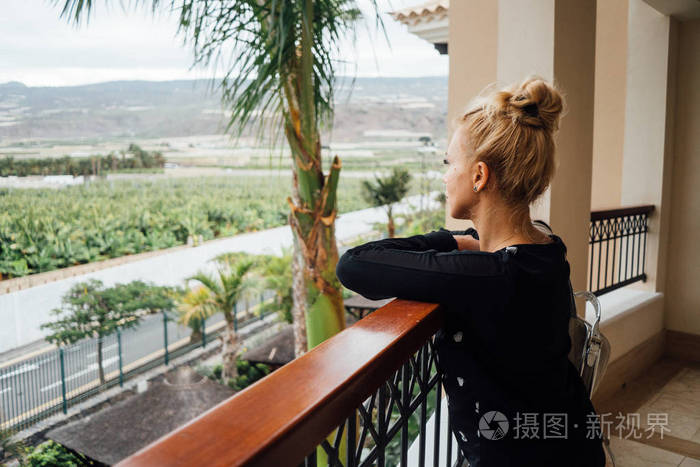 阳台上靠栏杆的金发女郎的侧面观景与欣赏观