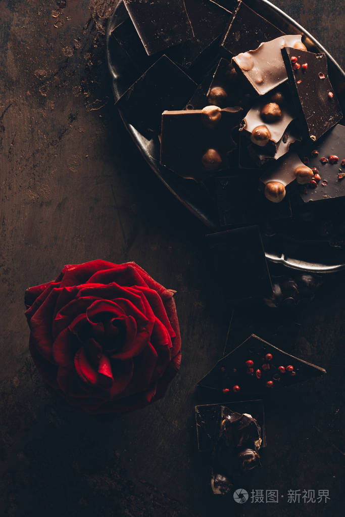 美丽的红玫瑰花和各式各样的美味巧克力片在黑暗的表面上的顶级视图