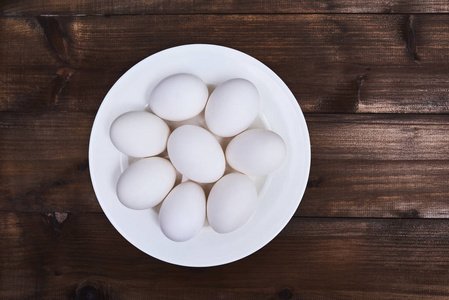 白色鲜鸡蛋在木制背景白色盘子上的顶部视图