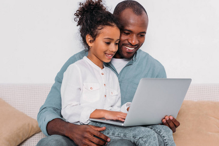 快乐的非洲裔美国人的父亲和女儿在家里使用笔记本电脑