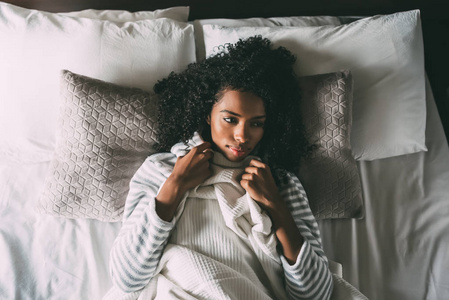 美丽体贴的黑人妇女与卷曲的头发躺在床上看着远离