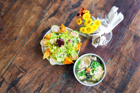 烟鲑鱼饺子沙拉和蘑菇鸡肉馄饨汤在一个白色的盘子和一个木桌上。中国菜。桌子上有花。带有复制空间的侧面视图