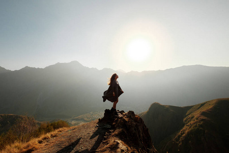 一个穿着飞天连衣裙的漂亮女孩站在俯瞰群山的悬崖上.照片