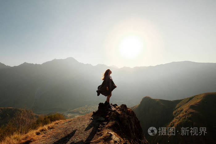 一个穿着飞天连衣裙的漂亮女孩站在俯瞰群山的悬崖上.