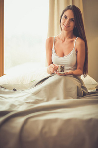 年轻女子坐在床上与一杯牛奶