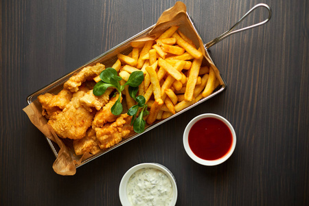 炸鸡块配薯条和木板上的不同调味汁照片