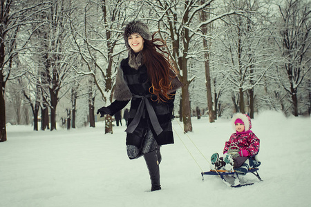 妈妈滚动女儿在雪橇在冬季公园