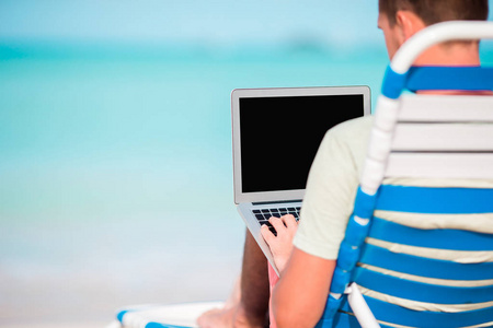 在热带加勒比海滩的年轻人与膝上型电脑。在男性手中关闭计算机