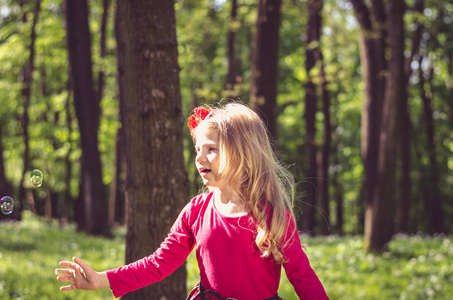 美丽的小金发女孩玩肥皂气泡户外在绿色的春天森林