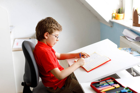 在家带眼镜的可爱的小男孩做家庭作业, 用五颜六色的钢笔写信