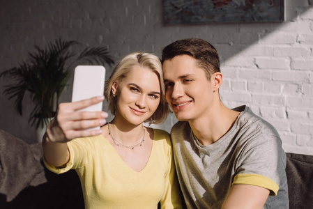微笑的夫妇采取自拍与智能手机在起居室
