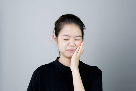 亚洲女孩穿着黑色休闲服装炫耀牙痛, 也许是因为没有保持良好的口腔健康。在灰色背景下给出柔和的光