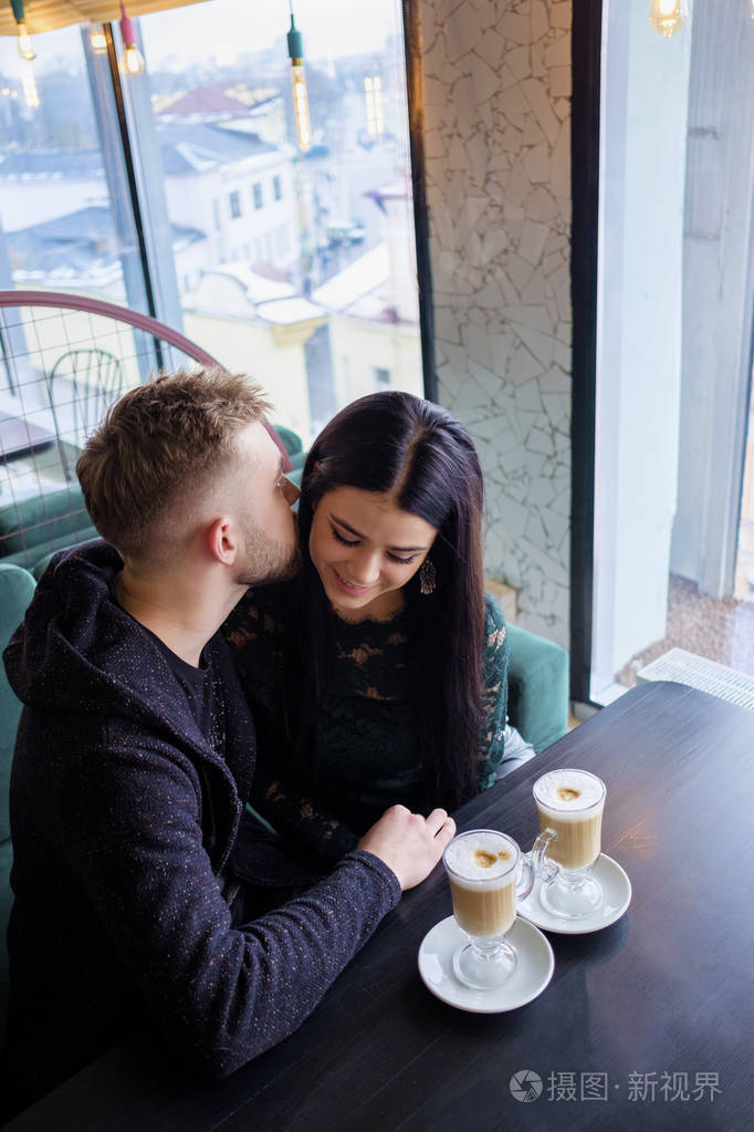 年轻可爱的情侣坐在咖啡馆, 喝 capuccino 和亲吻
