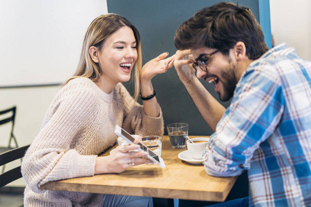 小情侣笑着在咖啡馆里使用智能手机