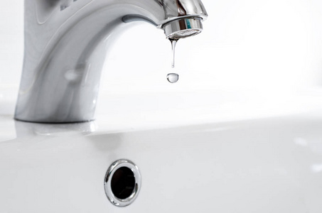 水龙头与一滴水对一个白色的水槽.漏水,节水照片
