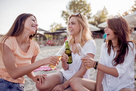 一群年轻的女性朋友坐在沙滩上, 用啤酒敬酒