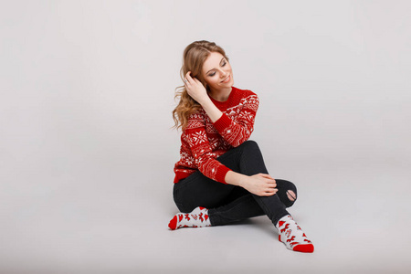 美丽的年轻女子在红色圣诞复古毛衣与袜子坐在地板上的工作室