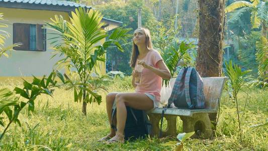 坐在亚洲乡村乡村和饮用水长凳上的年轻女子