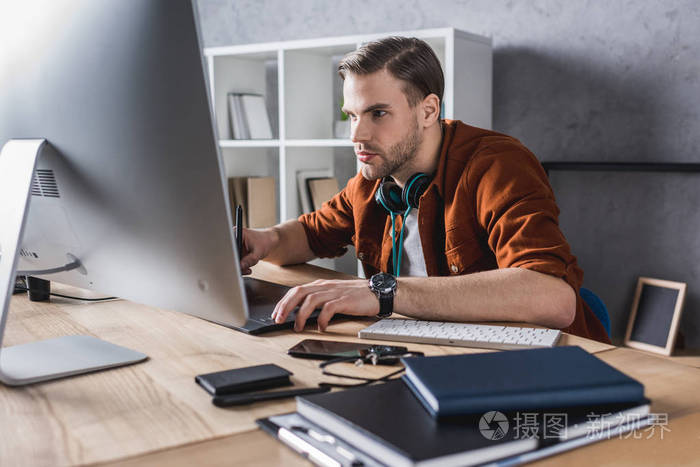 在现代办公室与计算机工作的英俊的年轻人