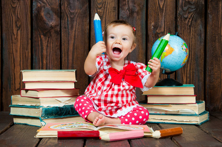 快乐一个漂亮的小女孩与眼镜和铅笔的背景下的书籍和地球仪