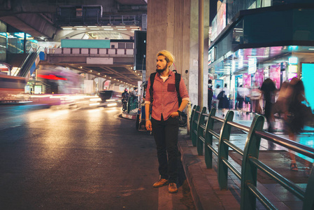 英俊的大胡子男子站在路边的街道, 而在夜间旅行在泰国曼谷市