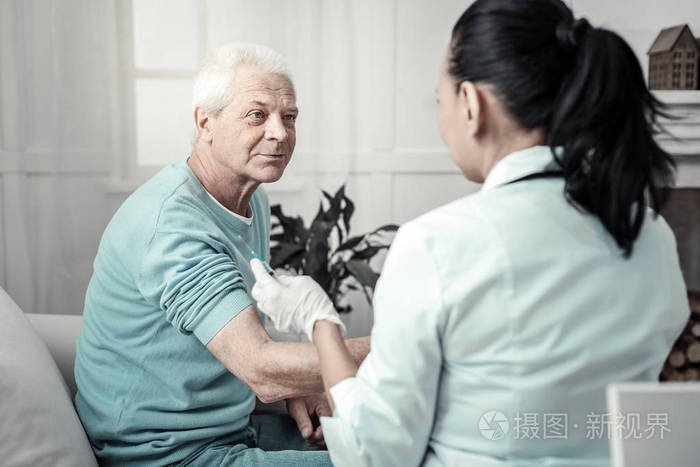 愉快的老人坐和准备他的胳膊为注射