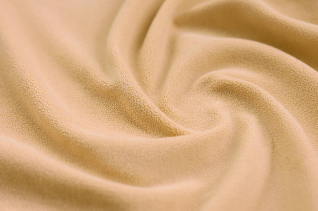 毛茸茸的橙色羊毛布的毯子。浅橙色软毛绒绒材料的背景与大量浮雕褶皱