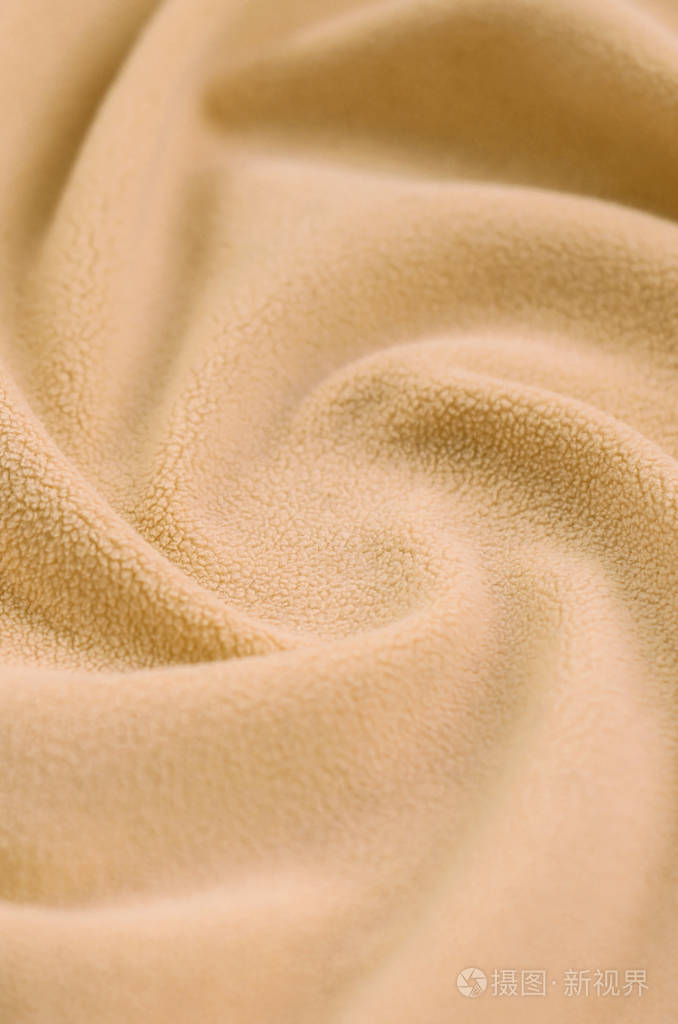 毛茸茸的橙色羊毛布的毯子.浅橙色软毛绒绒材料的背景与大量浮雕褶皱