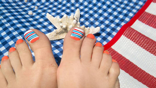 船用指甲设计。修脚与橙色和蓝色指甲油的女性脚特写在海上的格子日光浴在休息