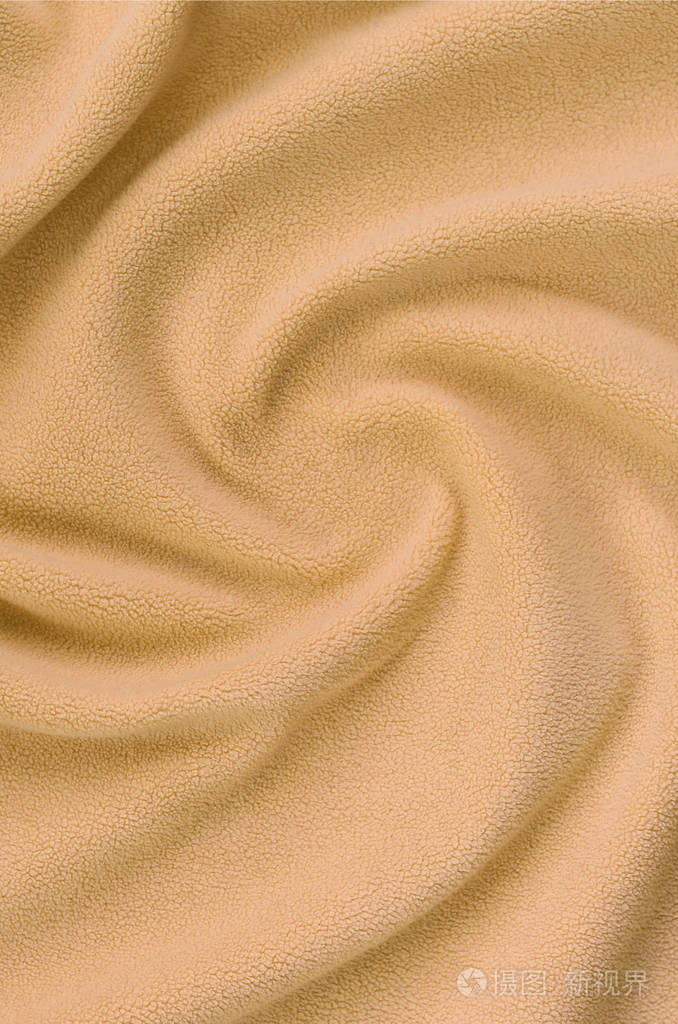 毛茸茸的橙色羊毛布的毯子.浅橙色软毛绒绒材料的背景与大量浮雕褶皱